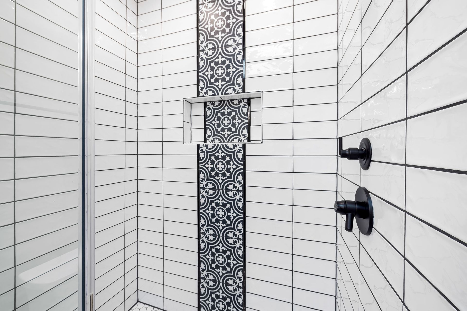 White tile shower with a black geometric mosaic accent stripe and matte black fixtures