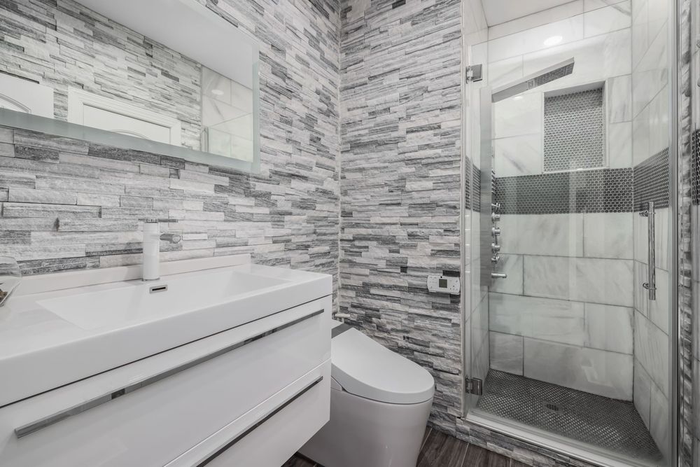 Finished modern bathroom with glass shower, stone wall and floating vanity
